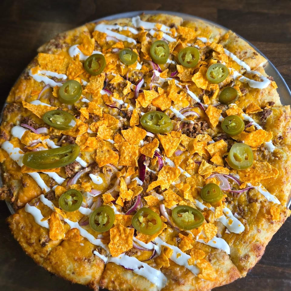 Cheesy nacho pizza topped with ground beef, crushed chips, jalapeños, red onion, and white sauce.