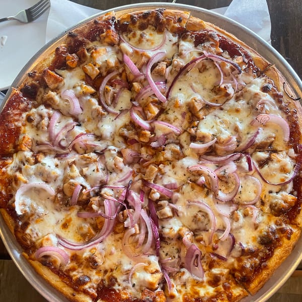 BBQ chicken pizza with melted cheese and red onion slices on a metal tray.